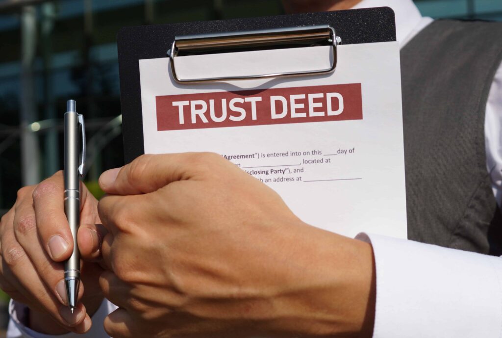 Person holding a clipboard with a trust deed document and pen, representing estate planning and legal agreements. Person holding a clipboard with a trust deed document and pen, representing estate planning and legal agreements.