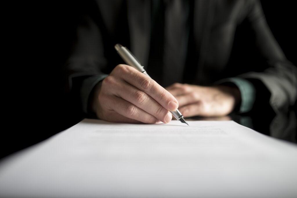 Business professional signing legal contract or agreement document with pen.