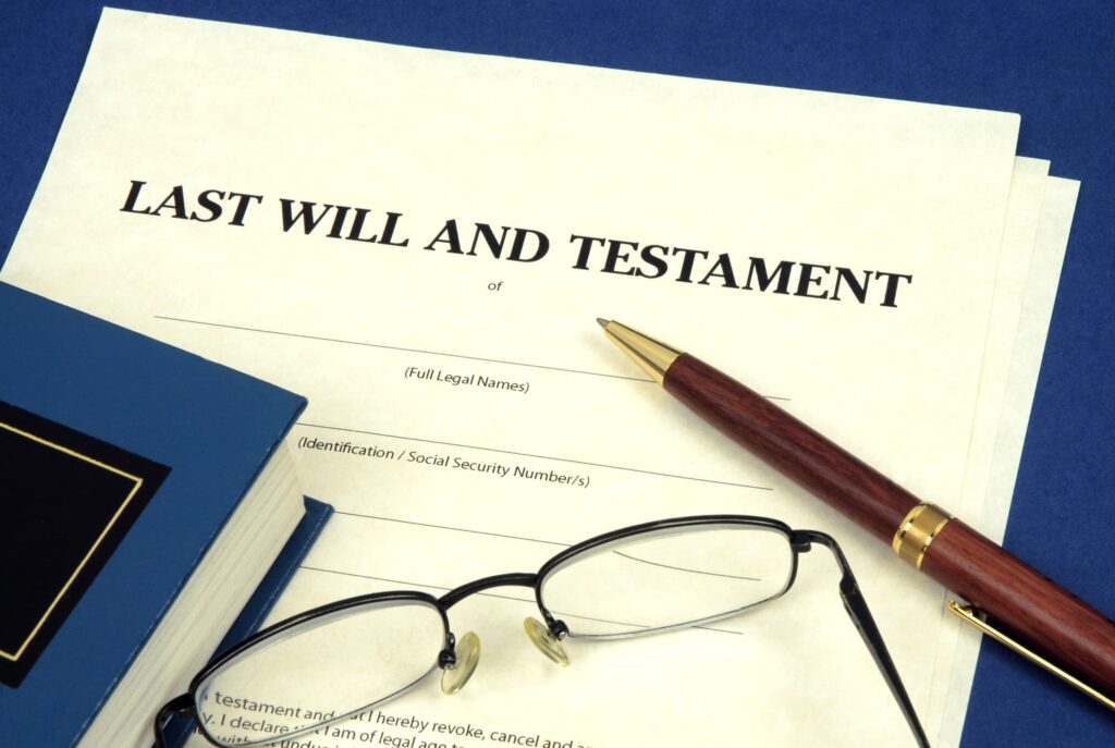 Last will and testament document with pen, eyeglasses, and legal book on desk.
