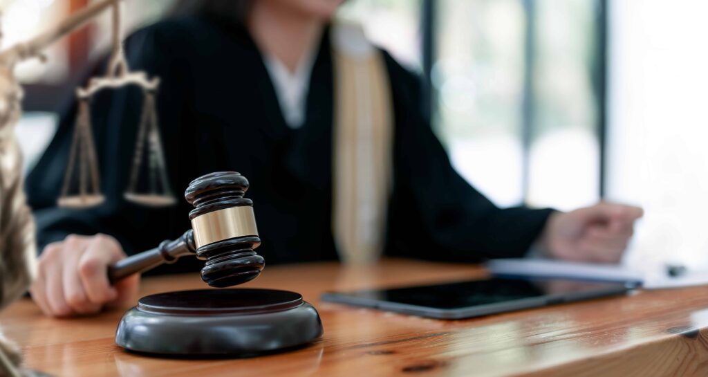 Judge holding gavel in courtroom with justice scales on wooden desk.