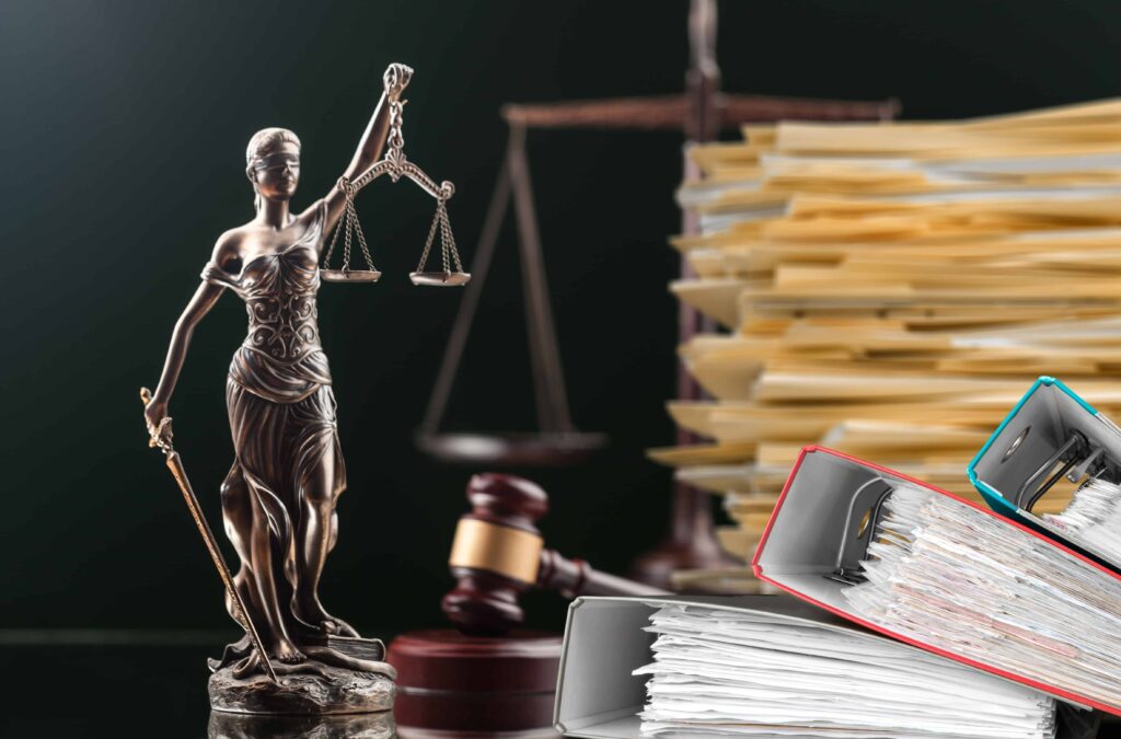 Lady Justice statue with gavel, legal scales, and stacks of case files on desk.