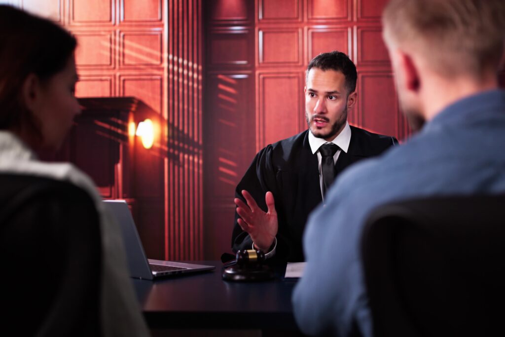 Judge speaking to two people during courtroom hearing or legal proceeding.
