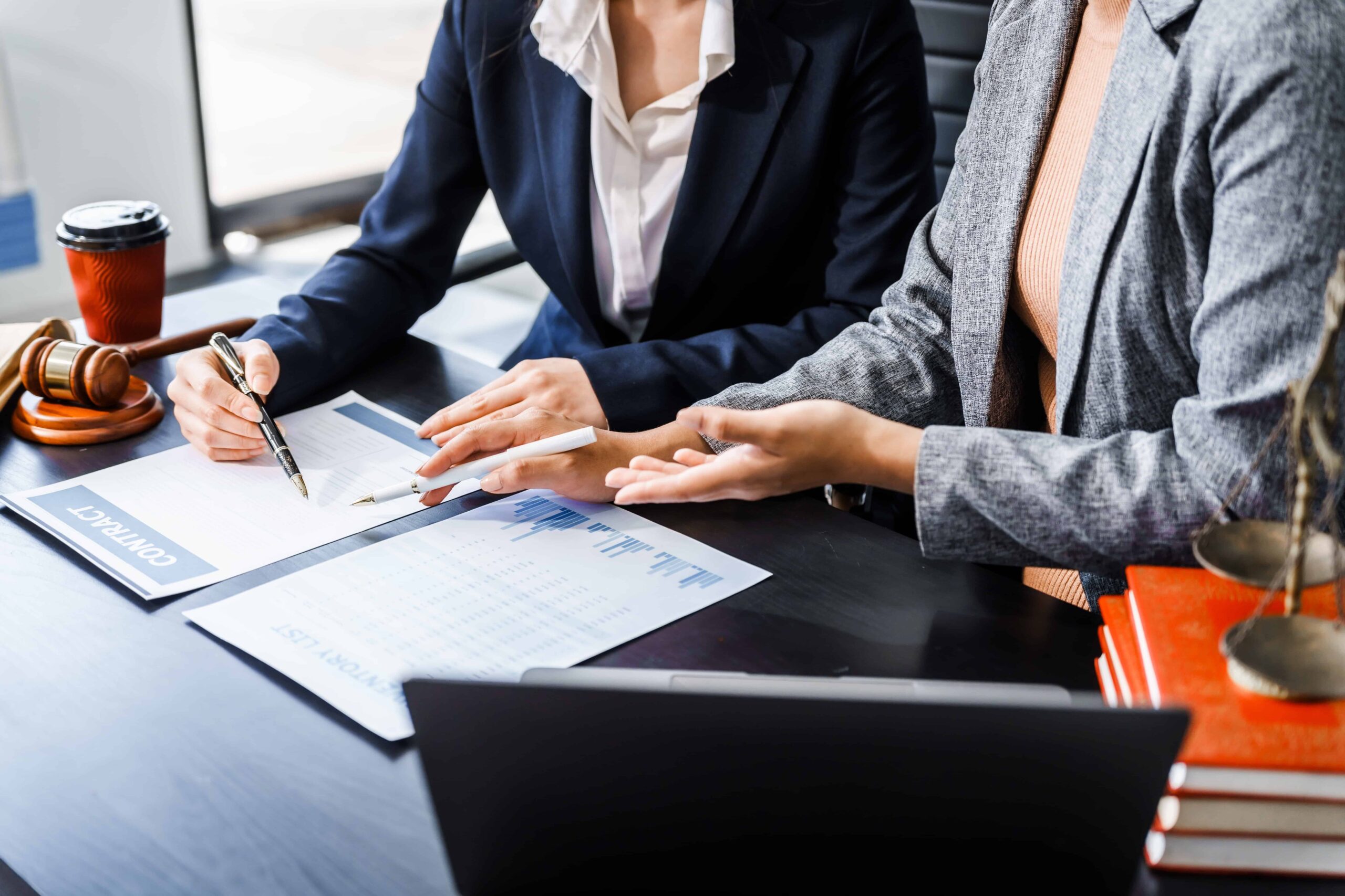 Business lawyers reviewing and signing contract documents at a desk with legal scales and gavel.