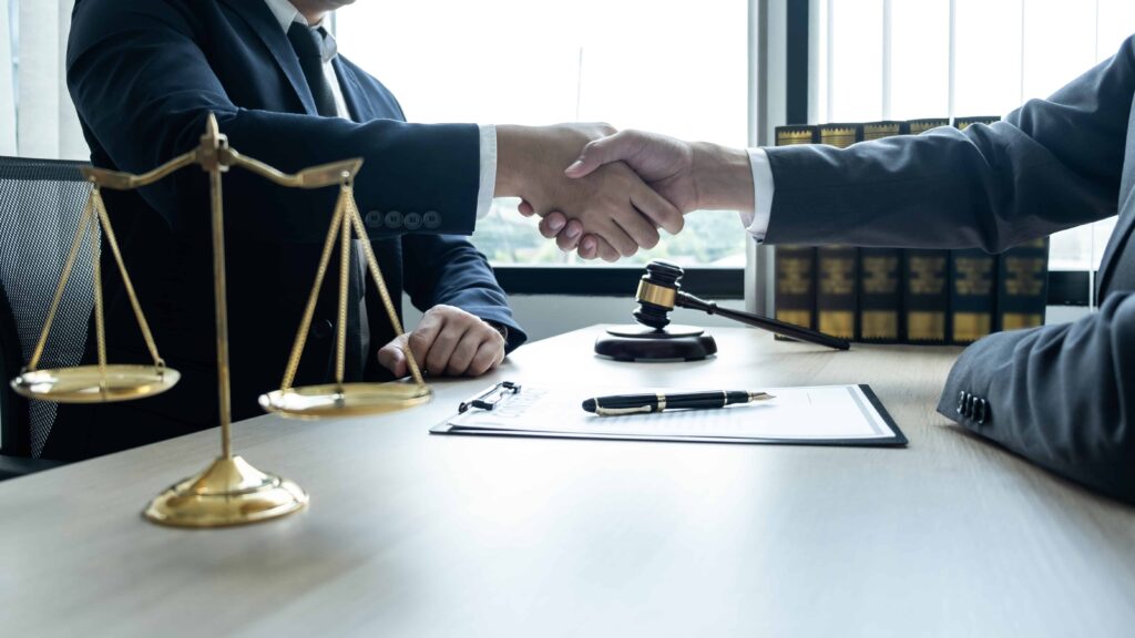 Lawyer and client shaking hands after successful legal consultation in law office with gavel and scales of justice on desk.